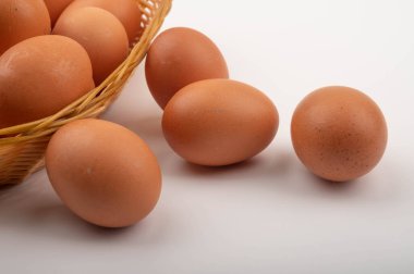 Hasır bir sepette tavuk yumurtaları ve beyaz arka planda saçılmış yumurtalar. Kapat.