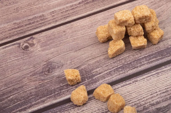 Pieces of brown cane sugar on a wooden background. Close up