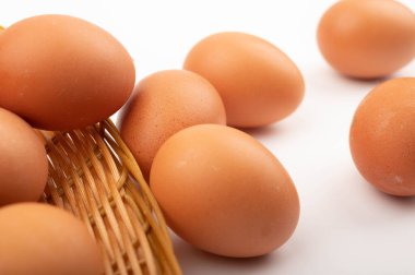Hasır bir sepette tavuk yumurtaları ve beyaz arka planda saçılmış yumurtalar. Kapat.