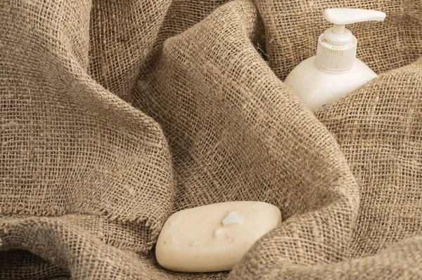 A piece of toilet soap and a dispenser with liquid soap on a background of coarse fabric. Close up. Clean hands prevention of COVID-19 infection