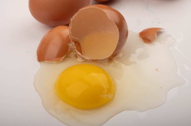 Kırık bir tavuk yumurtası ve beyaz arka planda dağınık yumurtalar. Kapat.