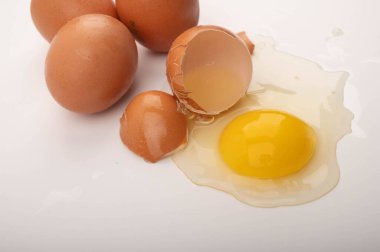 Kırık bir tavuk yumurtası ve beyaz arka planda dağınık yumurtalar. Kapat.