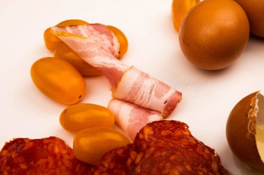 Sosis ve pastırma dilimleri, domates ve tavuk yumurtaları beyaz arka planda. Kapat.