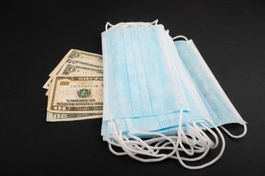 Siyah arka planda tek kullanımlık tıbbi maskeler ve dolar banknotları. Tek kullanımlık tıbbi maskeler COVID-19 enfeksiyonunun önlenmesidir. Görüntüyü algıla. Kapat..
