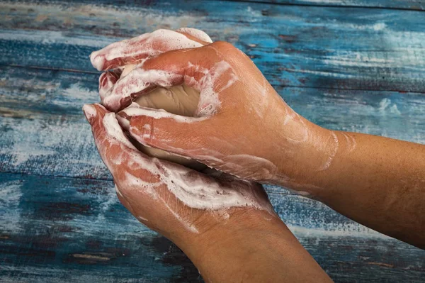 Someone is soaping their hands with a piece of toilet soap on a wooden background. Frequent hand washing with soap is a prevention of COVID-19 infection. Close up