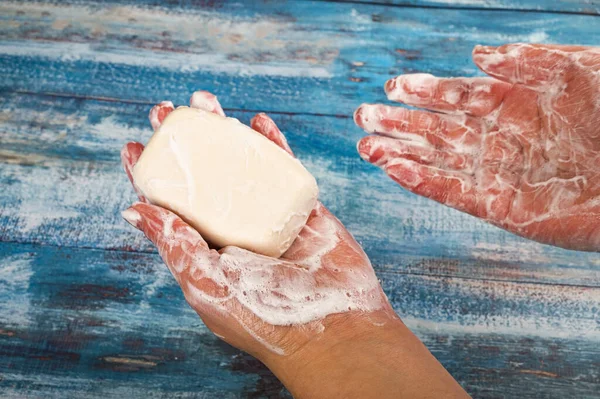 Someone is soaping their hands with a piece of toilet soap on a wooden background. Close up. Regular thorough hand washing with soap is a prevention of COVID-19 infection