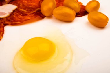 Kırık tavuk yumurtası, dağınık tavuk yumurtası, beyaz arka planda sosis, pastırma ve domates dilimleri. Kapat.