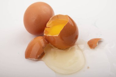 Kırık tavuk yumurtası ve tavuk yumurtaları beyaz arka plana saçılmış. Kapat.