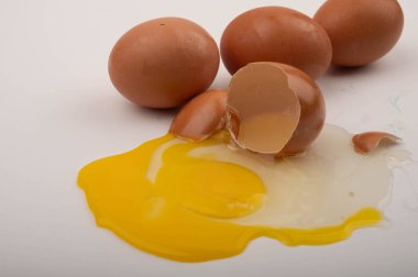 Kırık tavuk yumurtası ve tavuk yumurtaları beyaz arka plana saçılmış. Kapat.