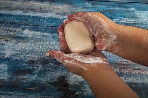 Someone is soaping their hands with a piece of toilet soap on a wooden background. Close up. Regular hand washing with soap is a prevention of COVID-19 infection