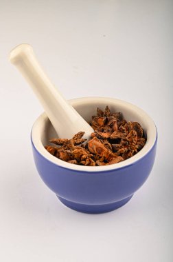 Beyaz arka planda bir tokmağı olan mavi seramik baharatlı havanda yıldız anason. Kapat.