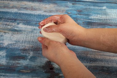 Birisi ahşap arka planda bir parça tuvalet sabunuyla ellerini sabunluyor. Kapatın. Kişisel hijyen kurallarına uymak COVID-19 enfeksiyonunun önlenmesidir.