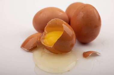 Kırık bir tavuk yumurtası ve beyaz arka planda dağınık yumurtalar. Kapat.