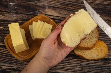 Birisi taze buğday ekmeğine bıçakla biraz tereyağı, ahşap tereyağı kabına bir parça tereyağı ve ahşap zemine taze buğday tostu sürer. Kapat.