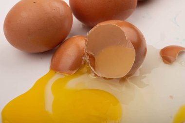 Kırık bir tavuk yumurtası ve beyaz arka planda dağınık yumurtalar. Kapat.