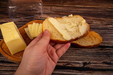 Birisi taze buğday ekmeğine bıçakla biraz tereyağı, ahşap tereyağı kabına bir parça tereyağı ve ahşap zemine taze buğday tostu sürer. Kapat.