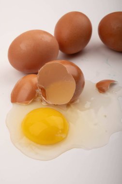 Kırık bir tavuk yumurtası ve beyaz arka planda dağınık yumurtalar. Kapat.