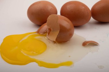Kırık bir tavuk yumurtası ve beyaz arka planda dağınık yumurtalar. Kapat.