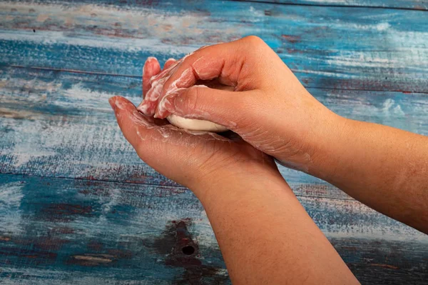 Someone is soaping their hands with a piece of toilet soap on a wooden background. Close up. Washing hands with soap is a prevention of COVID-19 infection