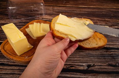 Birisi taze buğday ekmeğine bıçakla biraz tereyağı, ahşap tereyağı kabına bir parça tereyağı ve ahşap zemine taze buğday tostu sürer. Kapat.