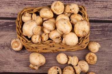 Hasır sepetin içinde genç mantarlar ve ahşap bir arka plana saçılmış mantarlar. Kapat.