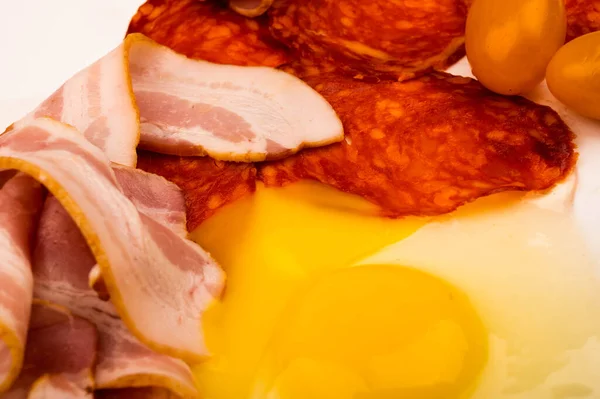 Um ovo de galinha quebrado sem casca, fatias de salsicha e bacon e tomates em um fundo branco. Fechar . — Fotografia de Stock