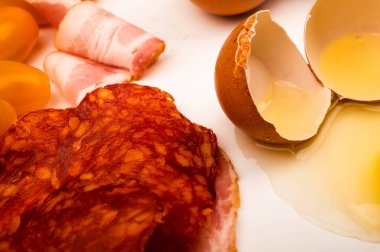Kırık tavuk yumurtası, sosis, pastırma ve beyaz arka planda domates dilimleri. Kapat.
