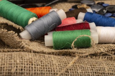 Kaba desenli çuval bezinin arka planına karşı birkaç bobin renkli dikiş ipi. Kapat.