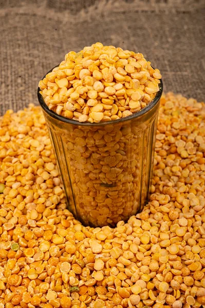 Yellow split peas in a cut glass and grits scattered on a background of coarse-textured burlap. Traditional cereals for making soups and porridge. Close up