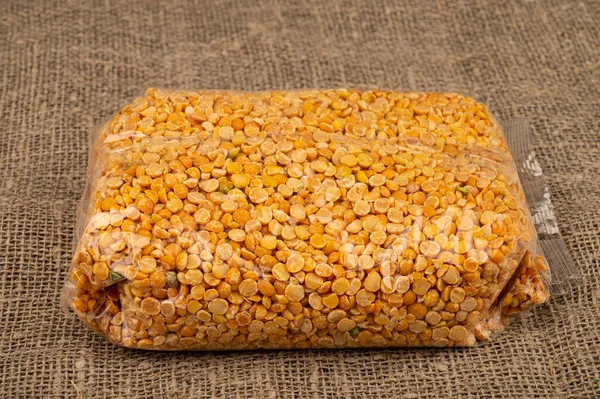 Yellow split peas in a cellophane bag on a background of coarse-textured burlap. Traditional grains for making soups and porridges. Close up — Stock Image Yellow Split Peas Cellophane Bag Background Coarse Textured Burlap Traditional Stock Image