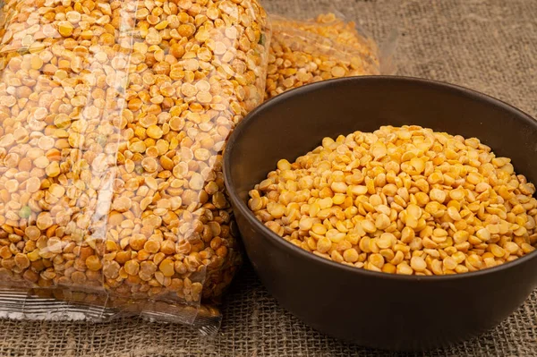 Yellow split peas in a cellophane bag and cereals in a ceramic bowl on a background of coarse-textured burlap. Traditional cereals for making soups and porridge. Close up — Stock Image Yellow Split Peas Cellophane Bag Cereals Ceramic Bowl Background Coarse Royalty Free Stock Photos