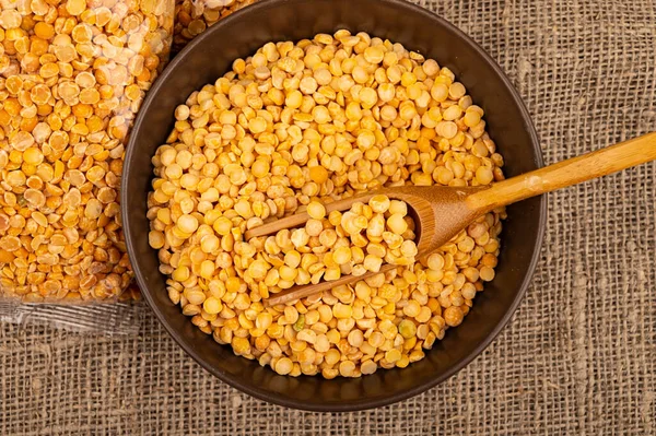 Yellow split peas in a cellophane bag and cereals in a ceramic bowl on a background of coarse-textured burlap. Traditional cereals for making soups and porridge. Close up — Stock Image Yellow Split Peas Cellophane Bag Cereals Ceramic Bowl Background Coarse Stock Photo