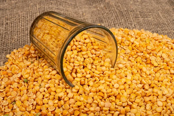 Yellow split peas in a cut glass and grits scattered on a background of coarse-textured burlap. Traditional cereals for making soups and porridge. Close up — Stock Image Yellow Split Peas Cut Glass Grits Scattered Background Coarse Textured Royalty Free Stock Photos