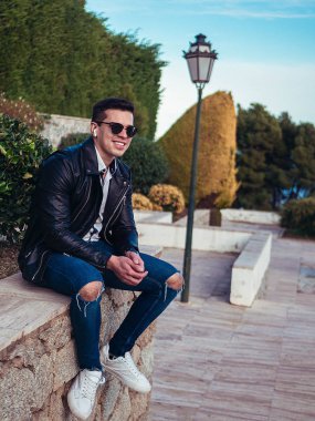 Genç adam zarif bir şekilde oturuyor ve günlük giysiler giyiyor.