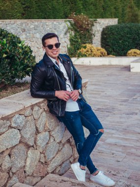 Genç adam zarif bir şekilde oturuyor ve günlük giysiler giyiyor.