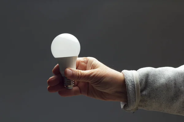 Enerji tasarrufu ampulü bir yetişkinin elinde.