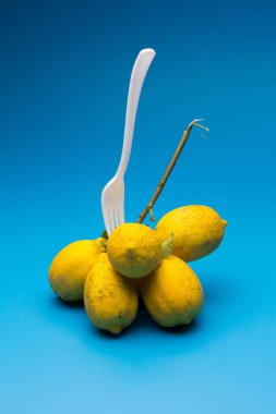 Asit aromalı ve vitaminlerle dolu sağlıklı limonlar, plastik çatal bıçak takımı, mavi arka planda citrus limonları..