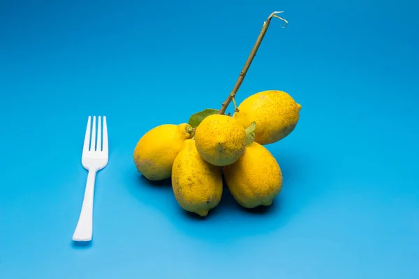 Healthy lemons with an acid flavor and full of vitamins, together with plastic cutlery; Citrus lemons on blue background.