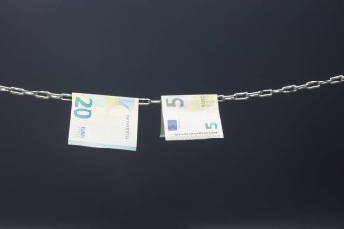 Money held in a chain or hung on a chain; paper money legal tender; Euros, currency of the European economic community, Common market.