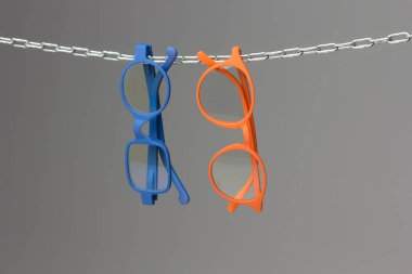 Colored glasses on a gray background and chain; glasses for vision correction; lenses to read or see from afar; Glasses can improve people's vision. clipart