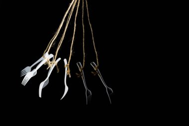 Birkaç beyaz plastik çatal, aynı görüntü ve siyah arkaplanda, bir ipte asılı..