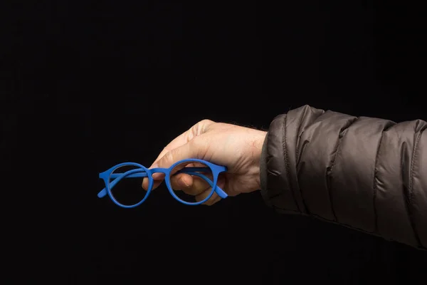 Visual health in the glasses, give away glasses for vision correction, colored designer glasses on a black background. Colored lenses in the hand of an adult person. Correction in the lenses of the glasses.
