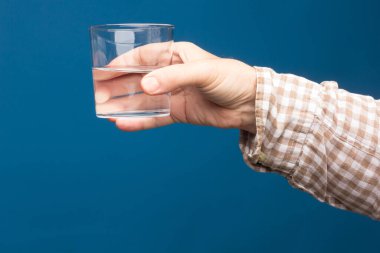 Bir insanın elinde şeffaf cam bardak. Bardak suyla ya da şeffaf sıvıyla dolu. İçme suyu