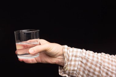 Bir insanın elinde şeffaf cam bardak. Bardak suyla ya da şeffaf sıvıyla dolu. İçme suyu