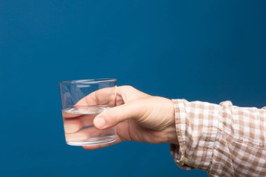 Bir insanın elinde şeffaf cam bardak. Bardak suyla ya da şeffaf sıvıyla dolu. İçme suyu