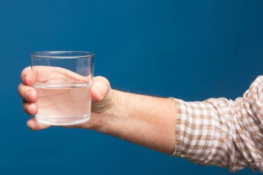 Bir insanın elinde şeffaf cam bardak. Bardak suyla ya da şeffaf sıvıyla dolu. İçme suyu