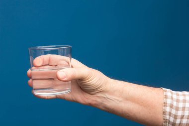 Bir insanın elinde şeffaf cam bardak. Bardak suyla ya da şeffaf sıvıyla dolu. İçme suyu