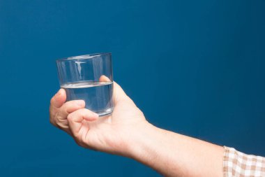 Bir insanın elinde şeffaf cam bardak. Bardak suyla ya da şeffaf sıvıyla dolu. İçme suyu