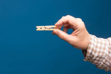 Ömür boyu ahşap mandal, mavi arka planda bir yetişkinin eline elbise asmak..