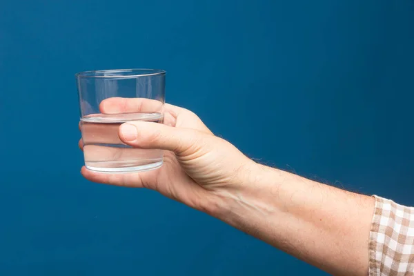 Transparent glass cup in the hand of a person. Glass filled with water or transparent liquid. Drinking water